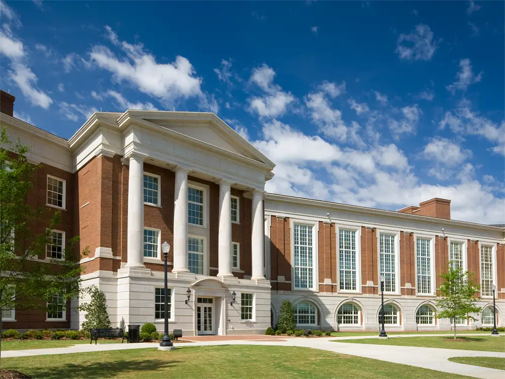 Green grass and trees adorn the front of a stately university.